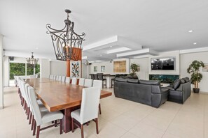 A spacious living area with a large wooden dining table, a gray sofa, and a chandelier.