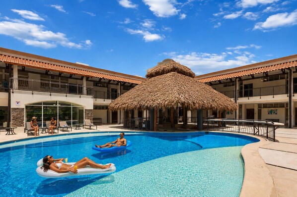A swimming pool with two people on inflatable floats, a thatched-roof structure, and a building with balconies. - 20BR Private Resort w/Chef Service and Driver (Herradura)