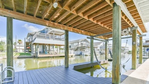 Une terrasse en bois avec une piscine, un espace couvert et une vue sur une maison dotée d’un balcon.