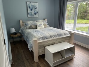 A bedroom with a bed, bedside table, lamp, and a view of the outdoors. - Relax and Revitalize at Sprucewood Cottage (Port Blandford)