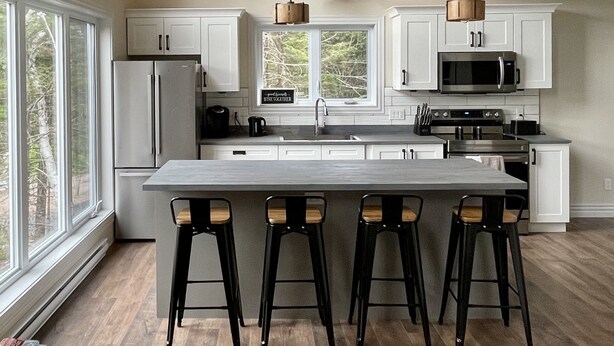Una cocina moderna con armarios blancos, una isla grande con taburetes de bar, un microondas y un refrigerador.