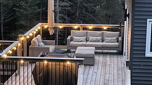 Una terraza de madera con asientos al aire libre, una escalera y vistas a una zona boscosa.