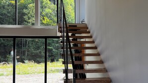 Un intérieur moderne avec un escalier en bois et de grandes fenêtres donnant sur une forêt.