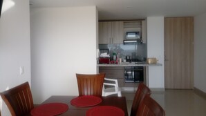 Een eetgedeelte met een tafel voor vier personen, een moderne keuken op de achtergrond met inbouwapparatuur, en een schuifdeurkast.