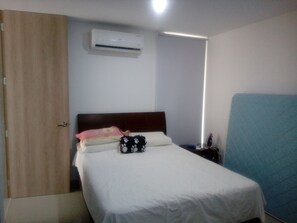 A hotel room with a single bed, a wooden wardrobe, an air conditioning unit, a bedside table with a lamp, and a blue partition. - PQALMETTO CONDOMINIO CLUB (Valledupar)