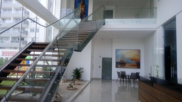 Een modern interieur met een glazen trap, een receptiegedeelte met een schilderij en uitzicht op het buiten gebouw.