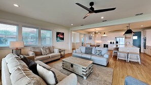 A spacious living room with a large sofa, a coffee table, and a ceiling fan. There is a kitchen area with modern appliances and a dining table. - Beachside Beauty (Palm Coast)