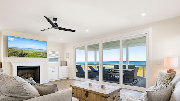 A spacious living room with a fireplace, comfortable seating, and a large sliding glass door leading to a balcony with a view of the ocean. - Beachside Beauty (Palm Coast)
