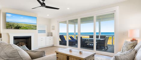 A spacious living room with a fireplace, comfortable seating, and a large sliding glass door leading to a balcony with a view of the ocean.