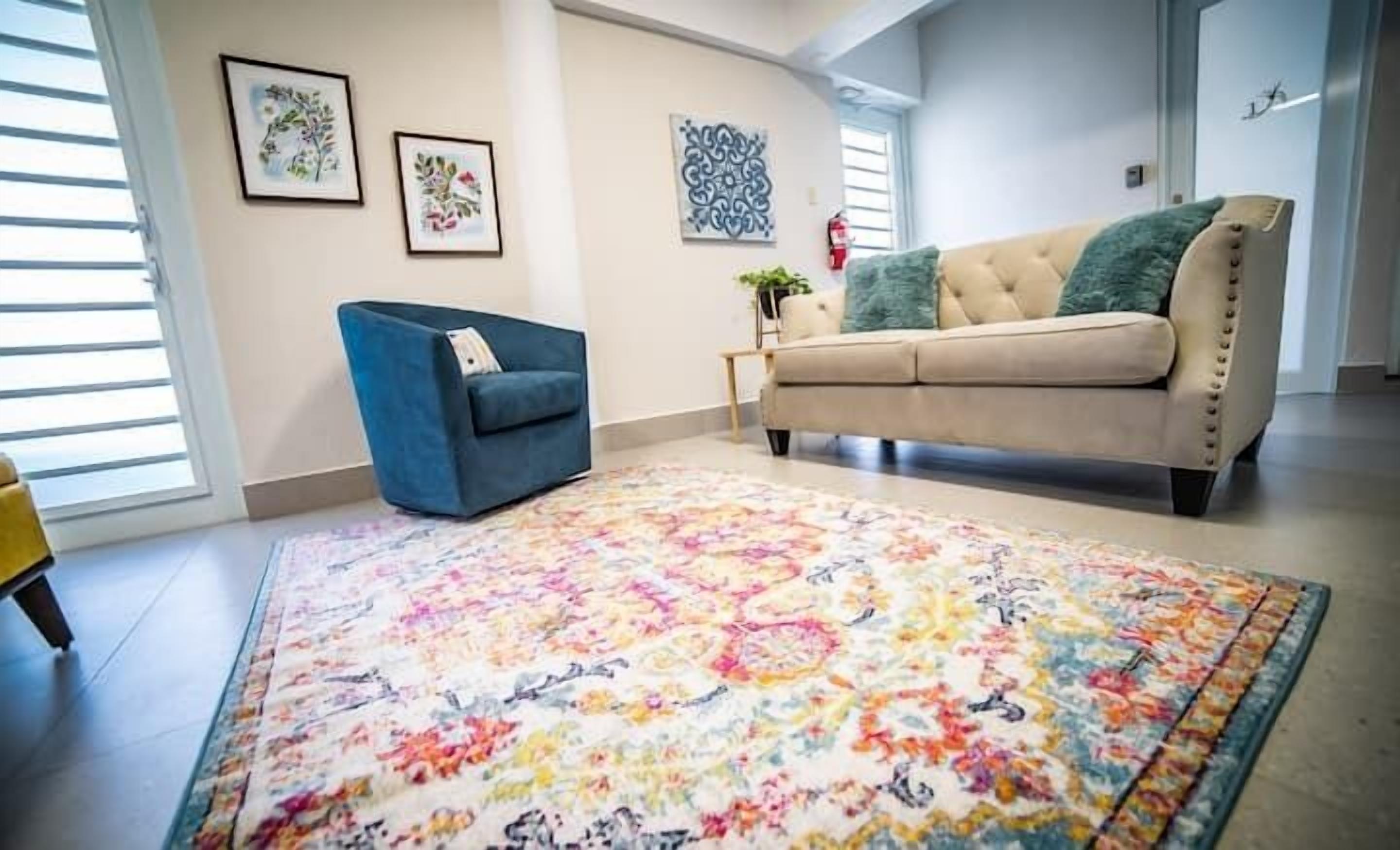 A living room with a beige sofa, a blue armchair, and a colorful rug.