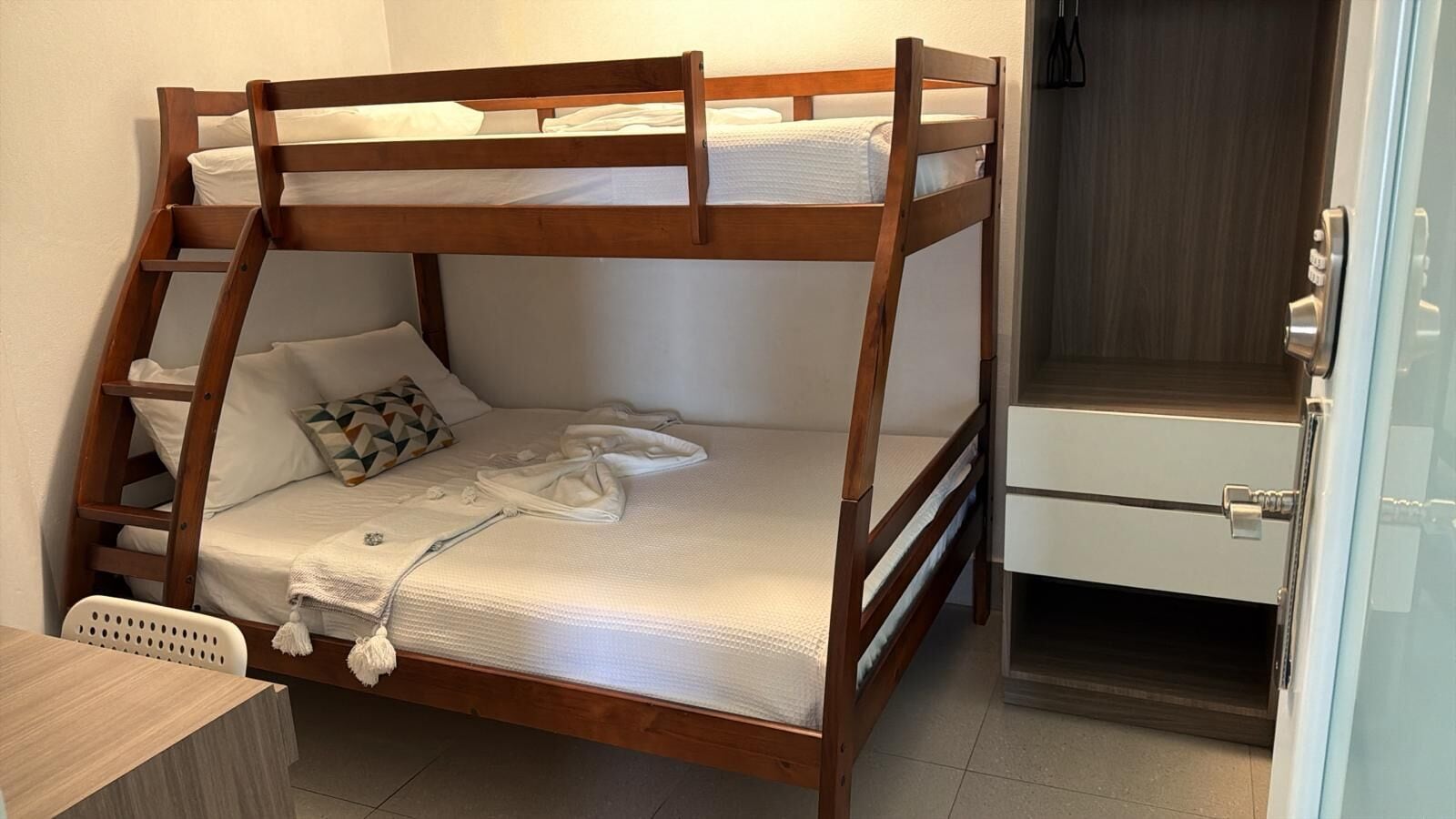 A bunk bed with a ladder, a desk, and a wardrobe in a room.