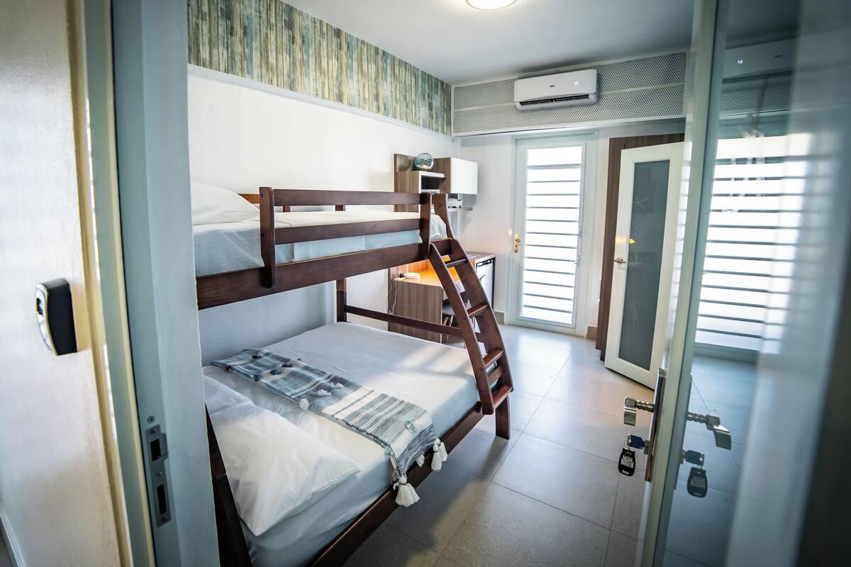 Ein Schlafzimmer mit Etagenbetten, einer Holzleiter, einem kleinen Schreibtisch und einer Tür zu einem Balkon.