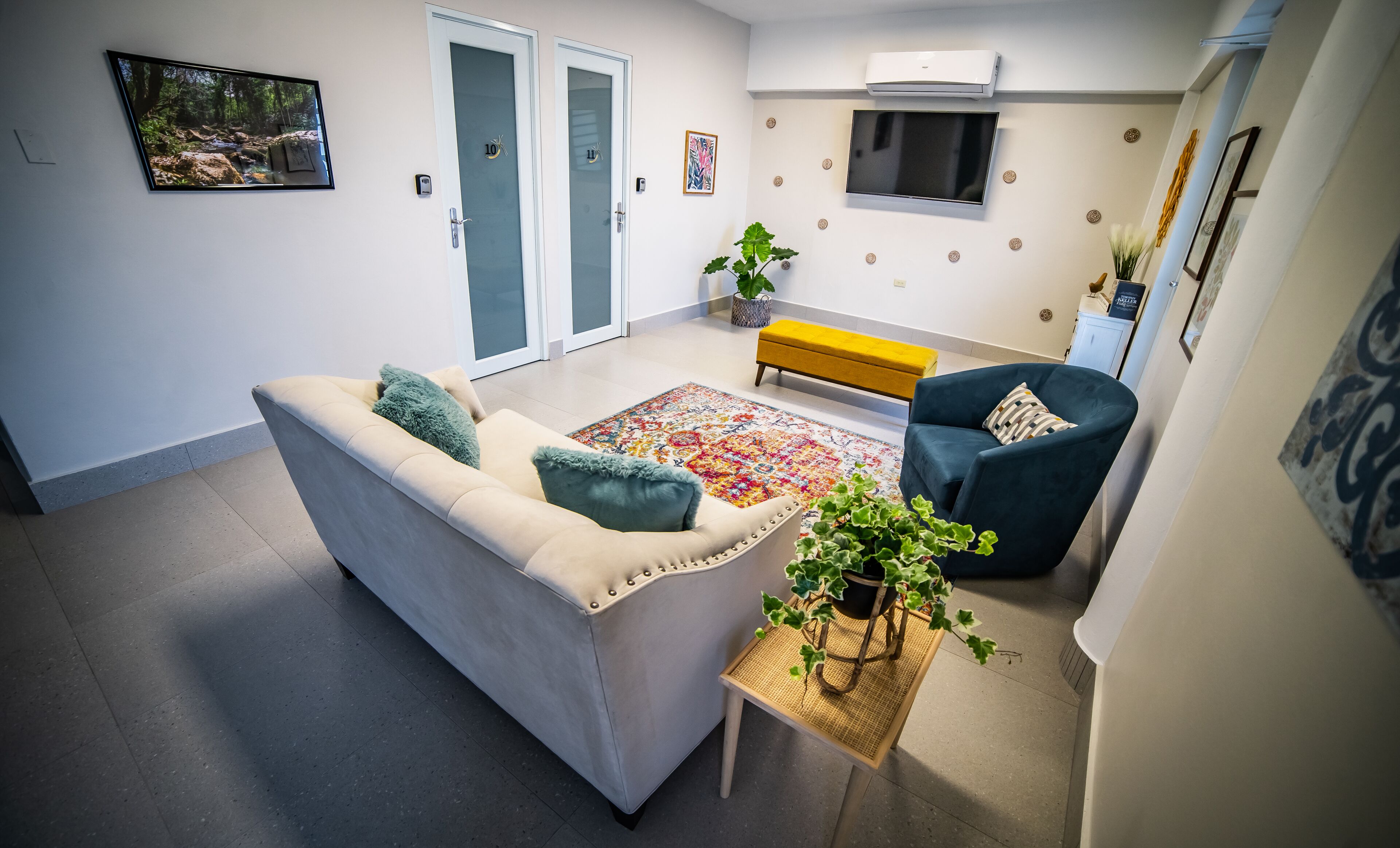 A modern living room with a beige sofa, a blue armchair, a yellow bench, and a colorful rug.