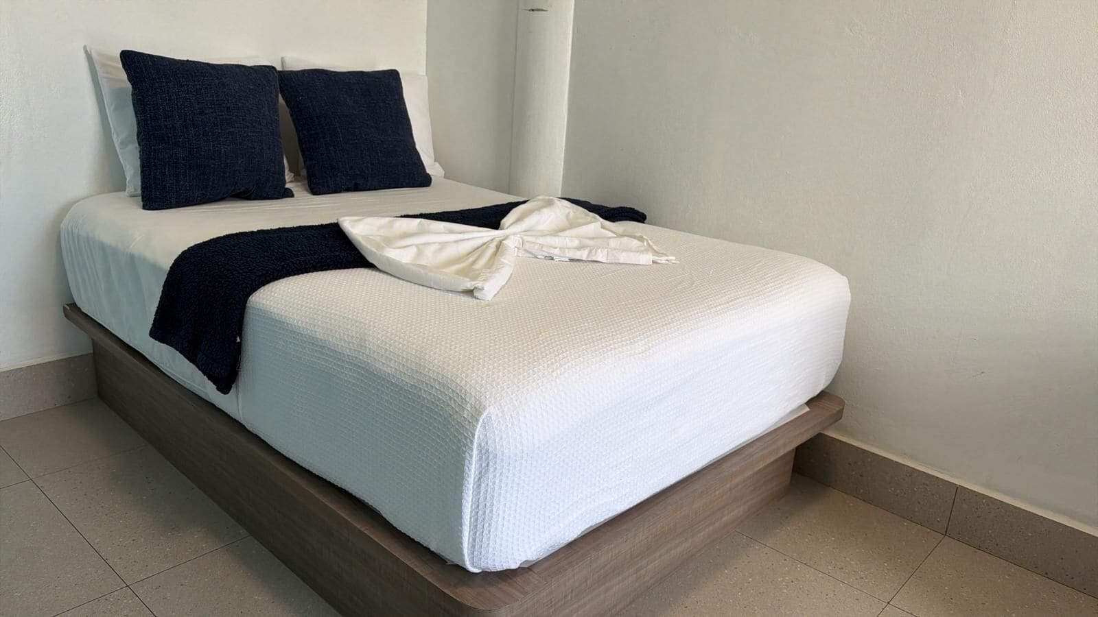 Un lit avec une couette blanche, deux oreillers foncés et un plaid foncé.