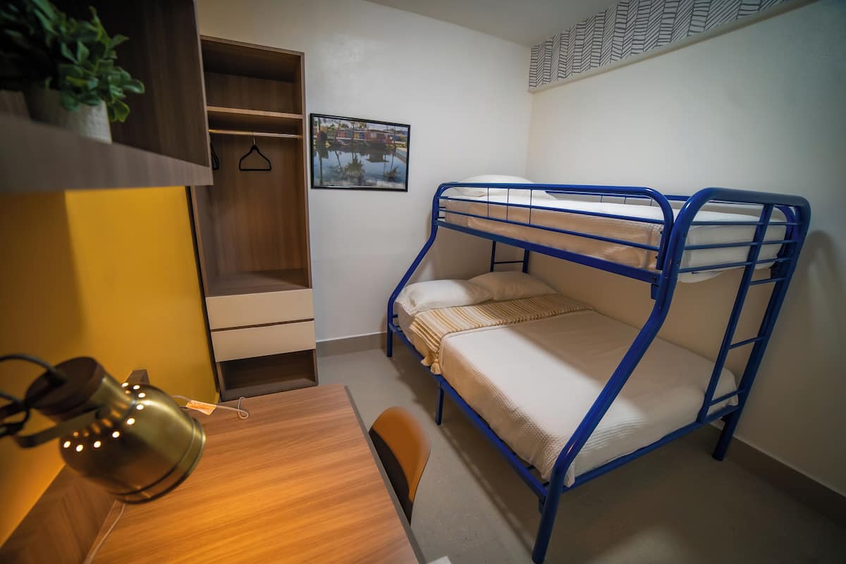 Ein Mehrbettzimmer mit Schreibtisch, einer Hängelampe und einem Bild an der Wand.