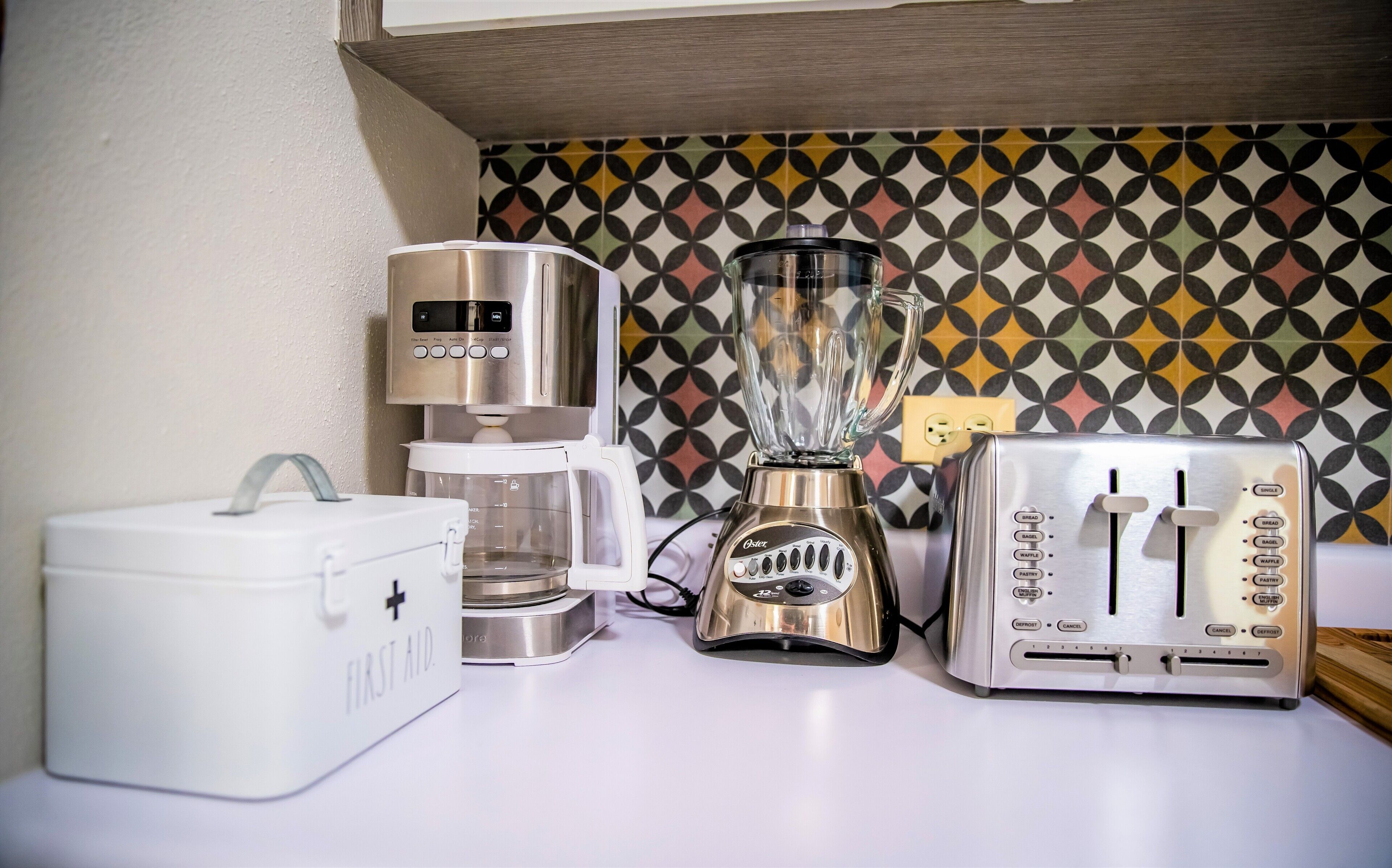 A kitchen with a coffee maker, blender, toaster, and a first aid kit.