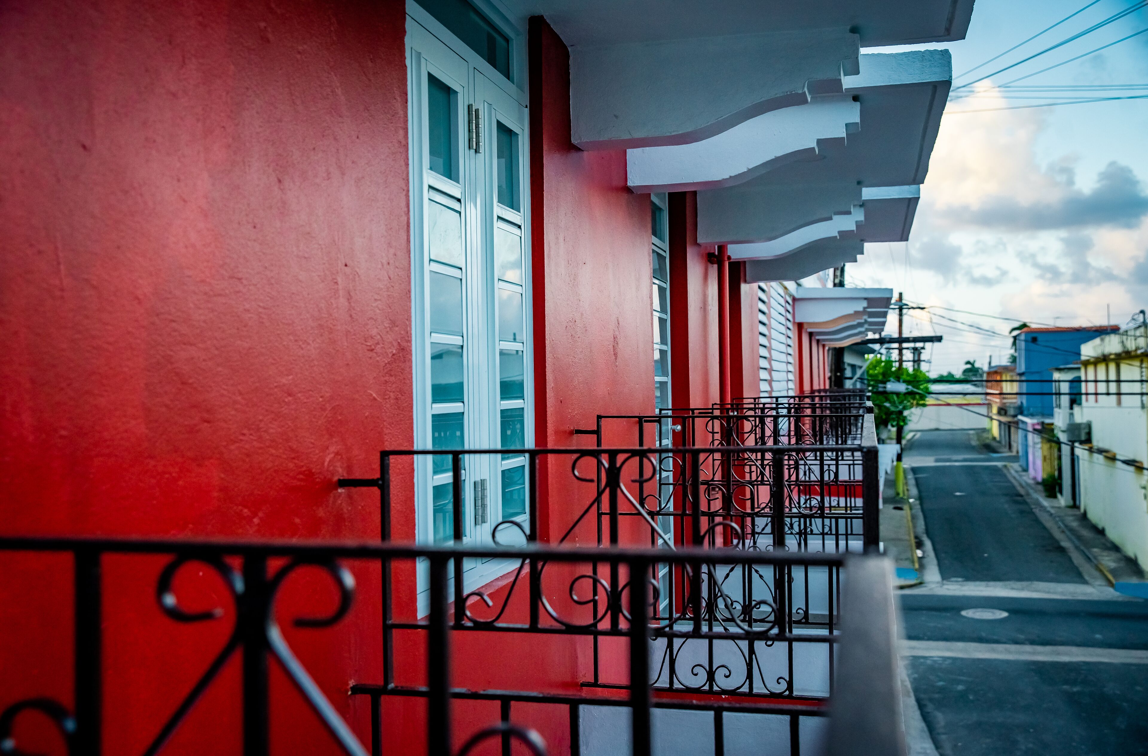 Una calle estrecha flanqueada por edificios, con balcones de barandillas metálicas y una pared roja en un lado.
