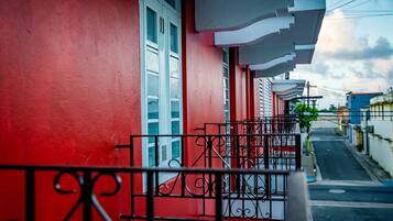 Una calle estrecha flanqueada por edificios, con balcones de barandillas metálicas y una pared roja en un lado.