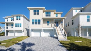 A modern multi-story residential building with a central staircase, multiple garage doors, and a well-maintained lawn. - Serenity Shores (Palm Coast)