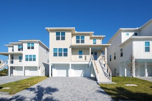 A modern multi-story residential building with a central staircase, multiple garage doors, and a well-maintained lawn. - Serenity Shores (Palm Coast)