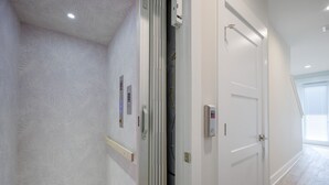 A hallway with white walls, a wooden floor, and a door with a control panel. - Serenity Shores (Palm Coast)