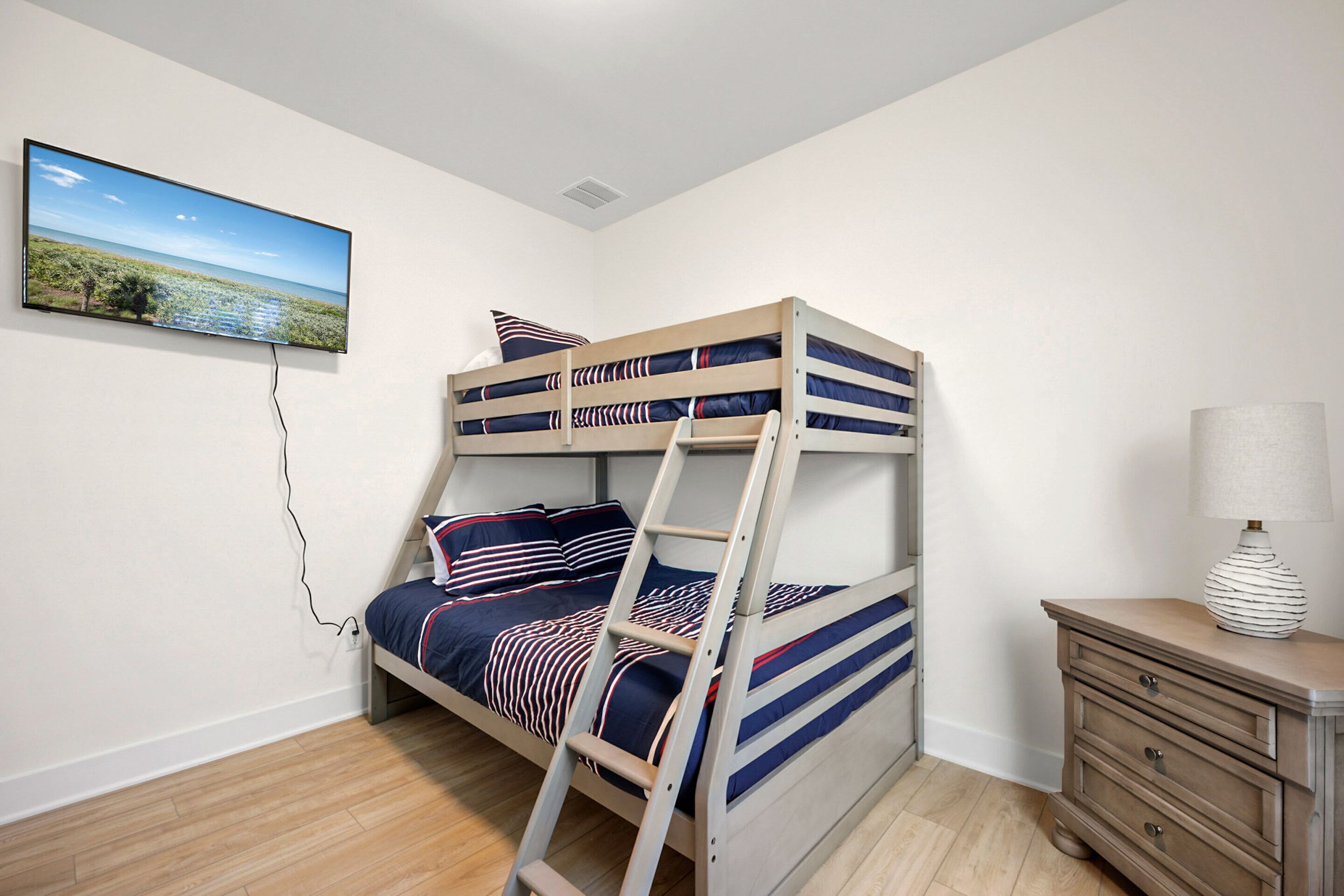 Una cama litera con un televisor montado en la pared superior, una escalera y una mesita de noche con una lámpara.