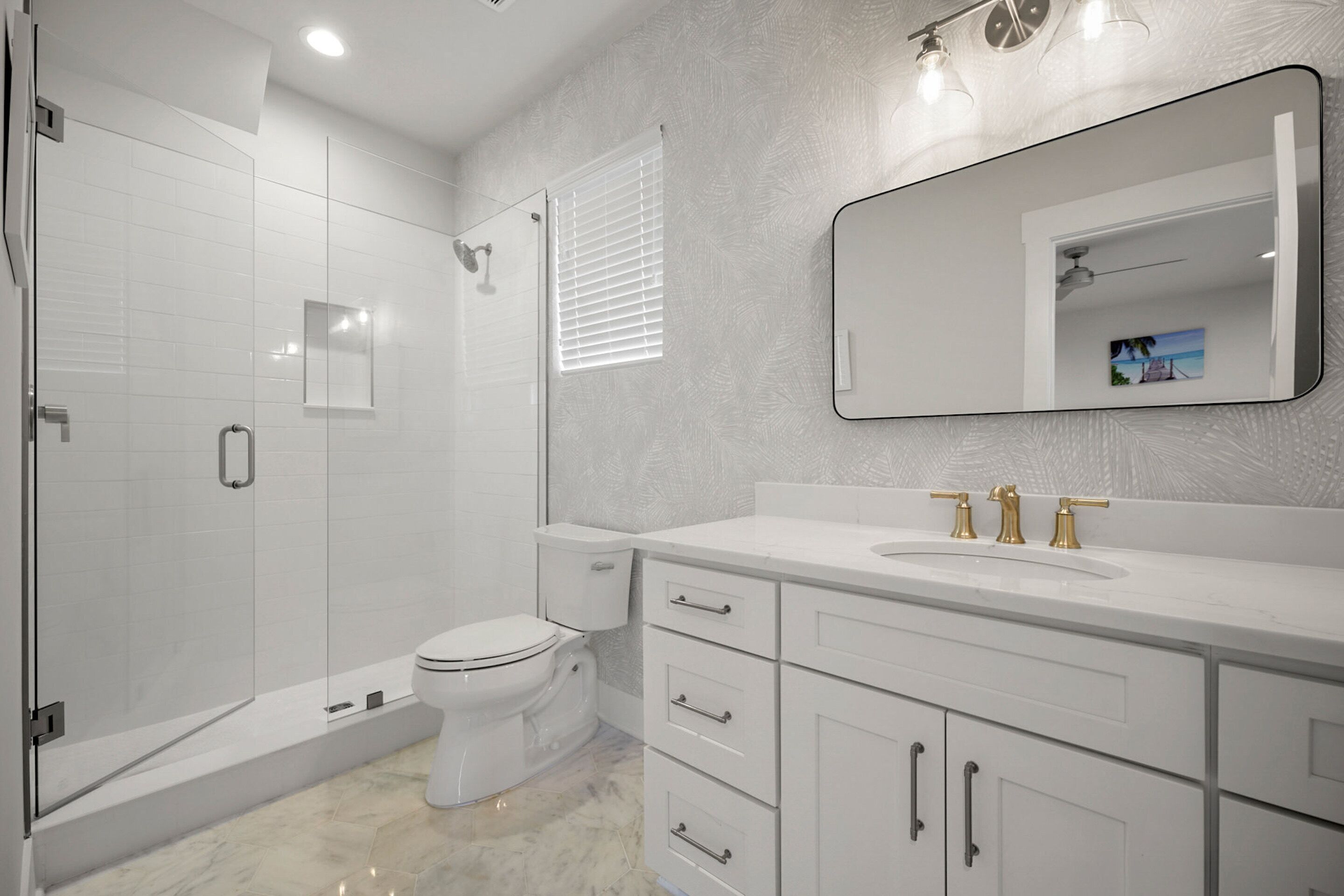 A modern bathroom with a glass-enclosed shower, a toilet, a sink with gold fixtures, and a large mirror.