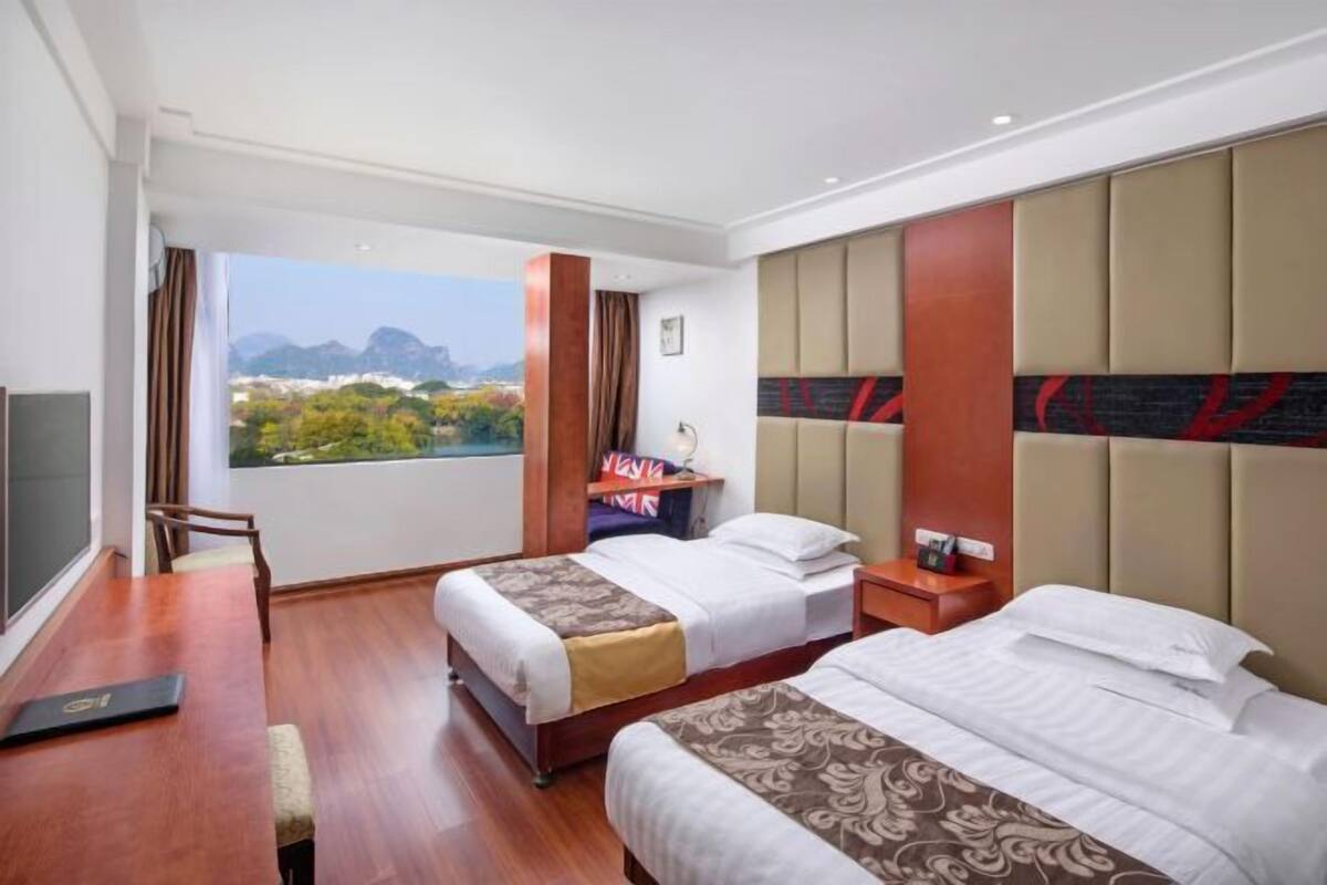 Ein Hotelzimmer mit zwei Betten, einem Schreibtisch und einem großen Fenster mit Bergblick.