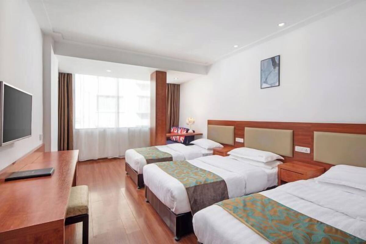 Ein Hotelzimmer mit zwei Betten, einem Schreibtisch, einem Fernseher und einem großen Fenster.
