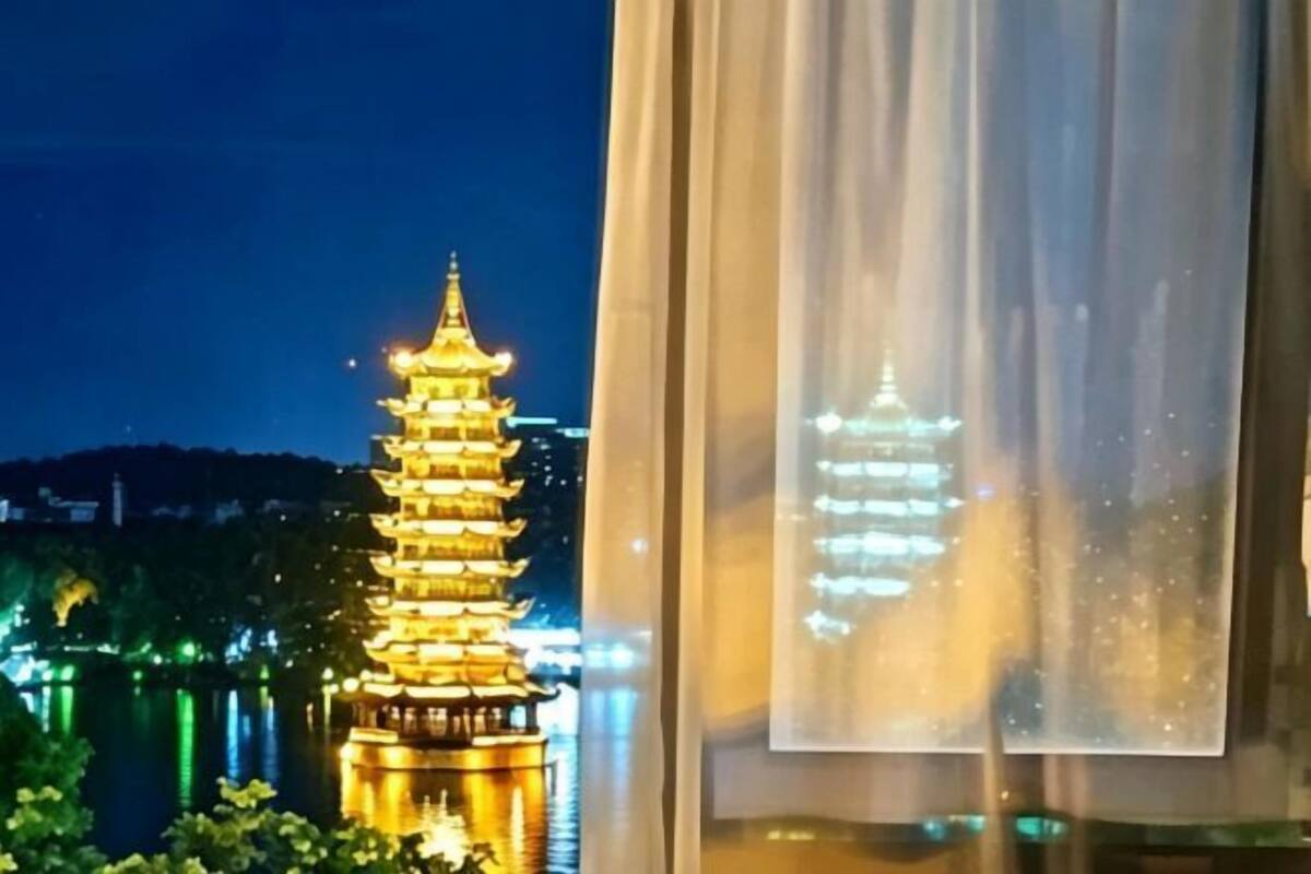 Ein pagodengleiches Gebäude mit mehreren Stufen, nachts beleuchtet, durch einen Vorhang drapierten Fenstersicht.