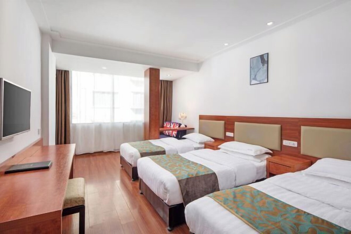 A hotel room with two beds, a desk, a TV, and a large window with curtains.