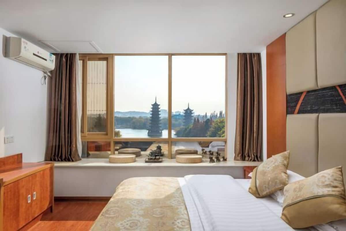 Ein Hotelzimmer mit Bett, einem Fenster mit Blick auf Pagoden, einem hölzernen Schminktisch und einem kleinen Tisch mit Dekorationen.