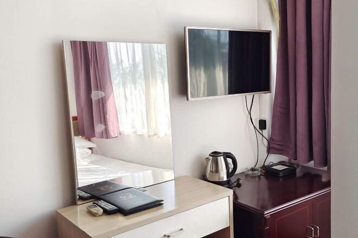 A hotel room with a bed, a bedside table with a book and a remote control, a television mounted on the wall, and a coffee maker on the table.