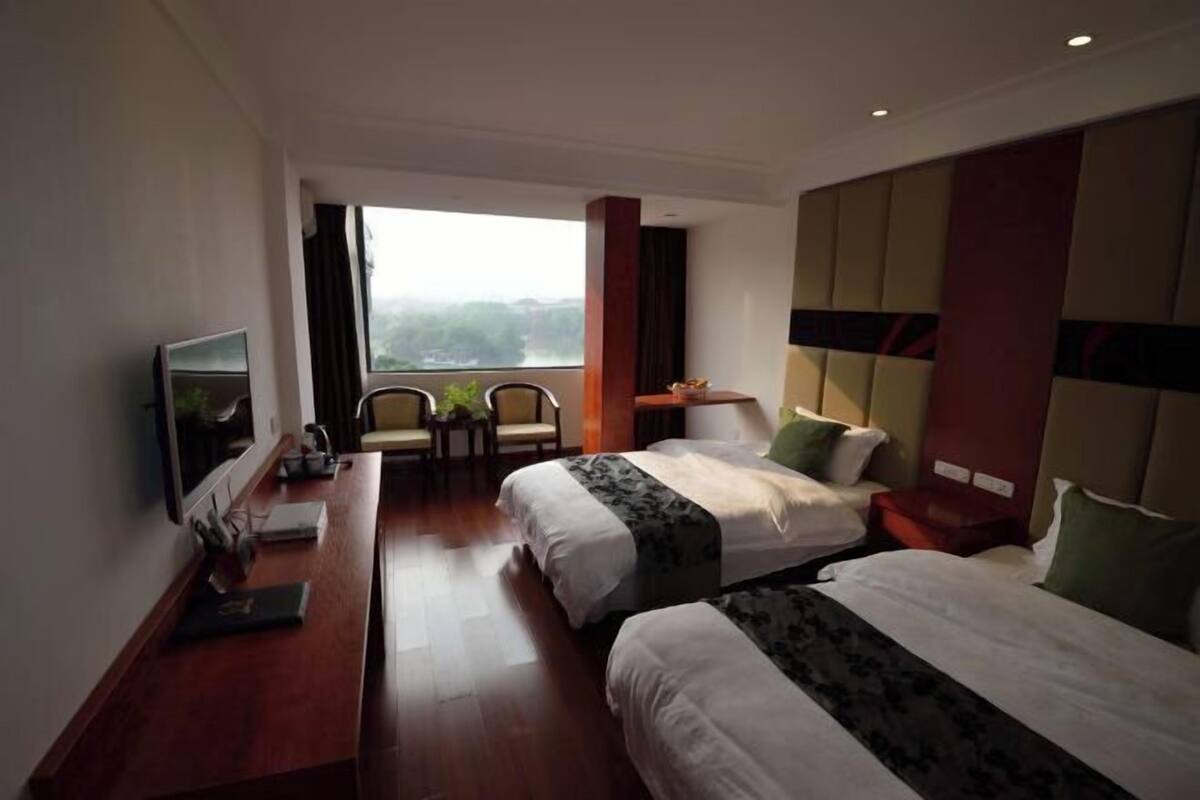 Ein Hotelzimmer mit zwei Betten, einem Schreibtisch, einem Sessel, einem Fernseher und Blick ins Freie.