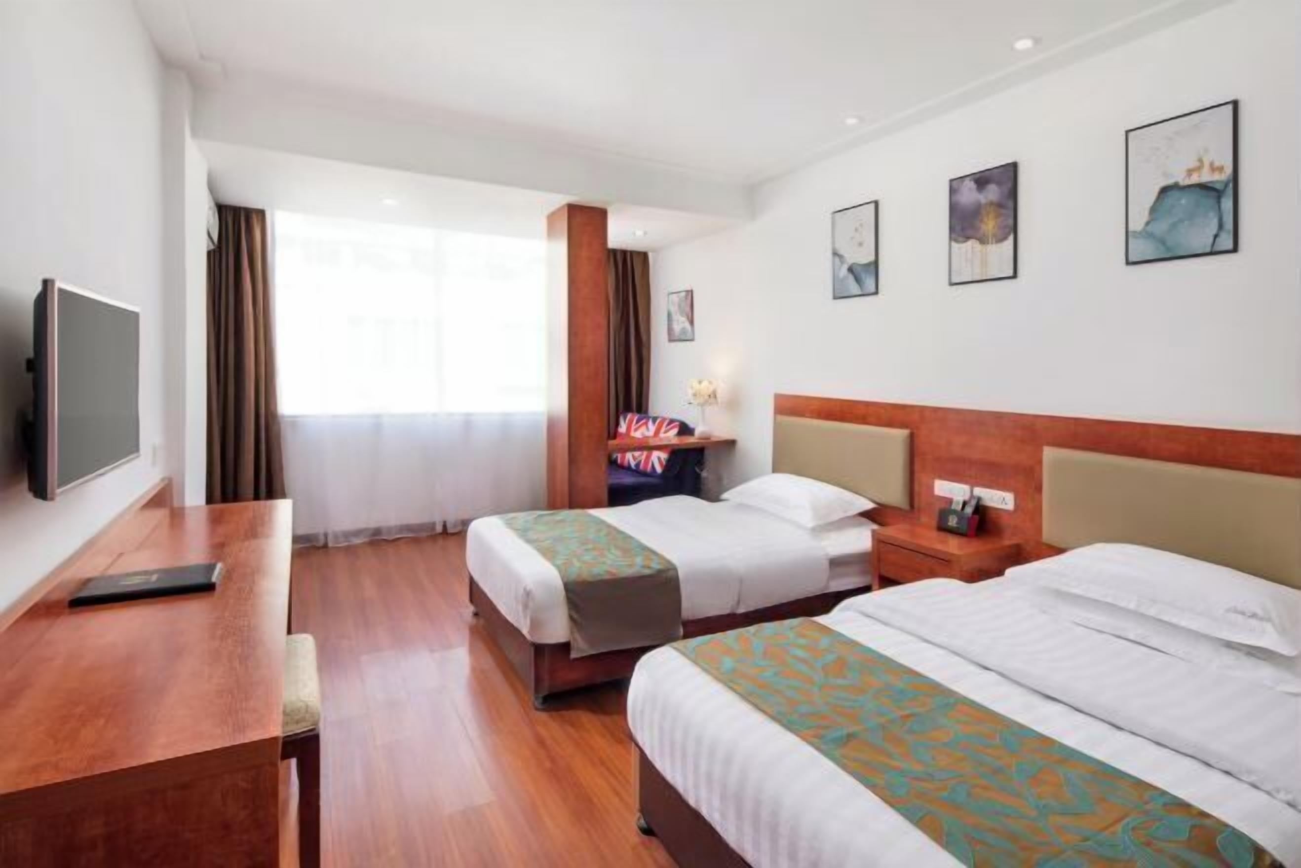 A hotel room with two beds, a desk, a TV, and artwork on the walls.