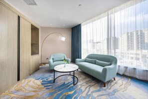 Une chambre d’hôtel moderne dotée d’une grande fenêtre, de deux fauteuils, d’une table basse ronde et d’un sol au motif marbré.