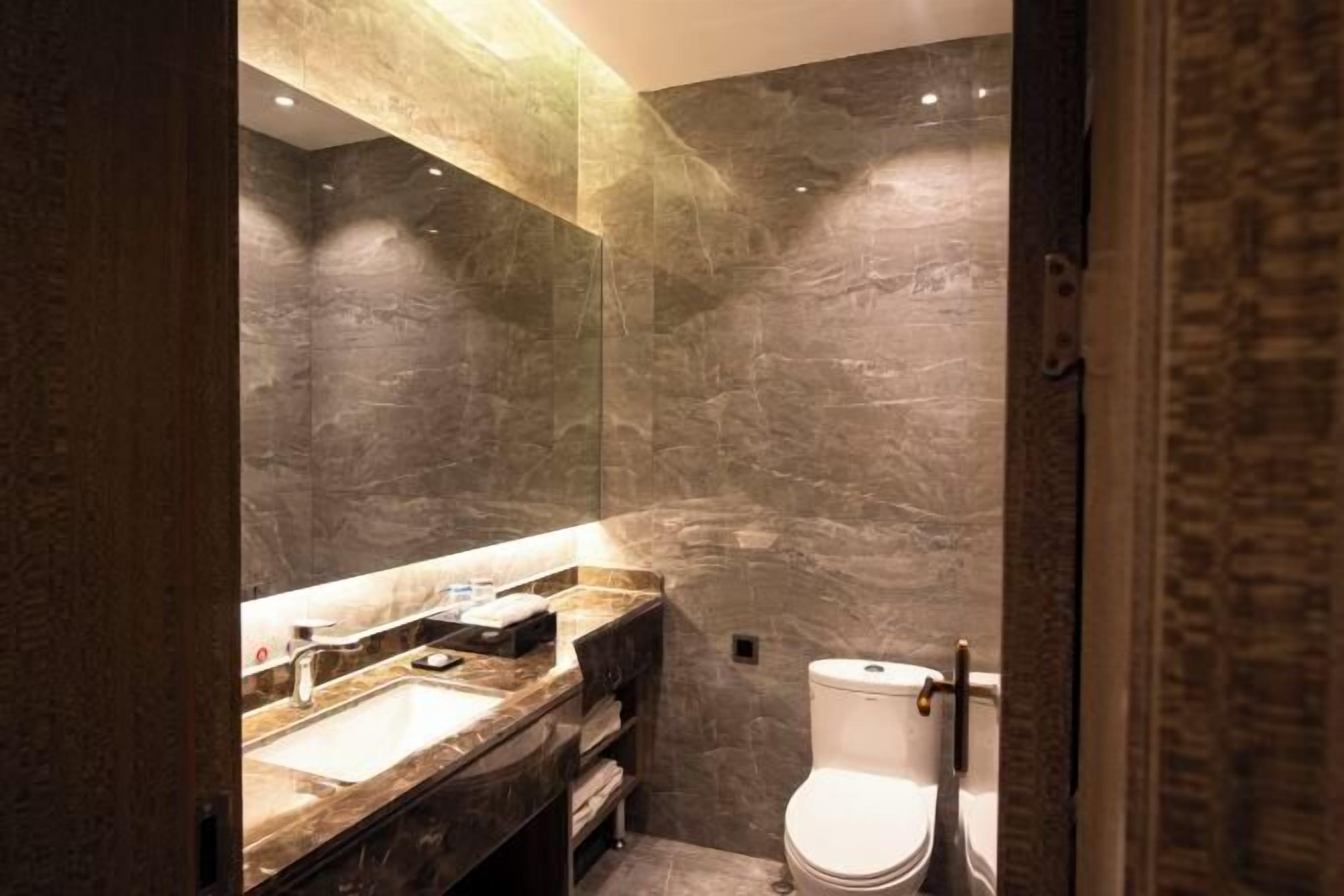 A modern bathroom with a marble sink, dark walls, and a white toilet.
