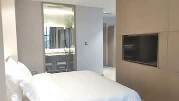 A modern hotel room with a large bed, a TV mounted on the wall, and a sliding door leading to a bathroom.