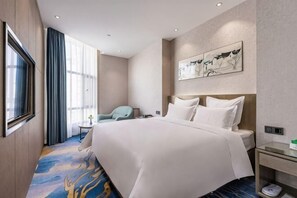 Quarto de hotel com uma cama grande, uma escrivaninha, uma cadeira e uma televisão.