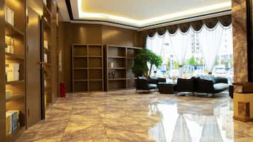 A lobby with a marble floor, bookshelves, a seating area with sofas, and a large window with curtains.