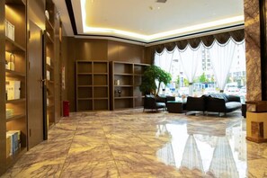 A lobby with a marble floor, bookshelves, a seating area with sofas, and a large window with curtains. - Horgos Hotel (Khorgas)