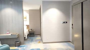 A hotel room with a bed, a desk, a trash bin, and a wardrobe.