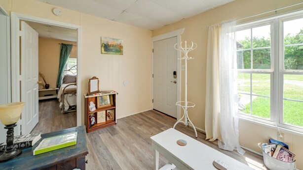 A room with a wooden floor, a white door, a bookshelf, a table, and a window with a view of greenery. - Serene McEwen Cottage ~ 2 Mi to Golf Course! (McEwen)