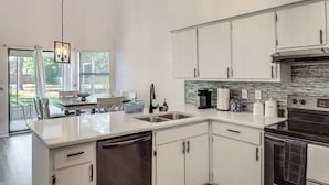 Een moderne keuken met witte kastjes, een vaatwasser, een oven en een koffiezetapparaat.