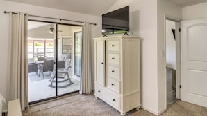 Een kamer met een schuifglasdeur naar een terras, een wit kastje en een flatscreen televisie die erboven is bevestigd.