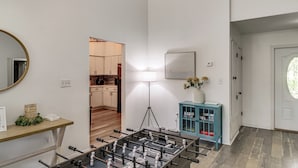 Een kamer met een tafelvoetbaltafel, een spiegel, een lamp, een kast en een deur naar een andere kamer.