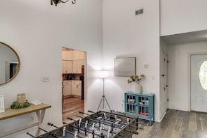 A room with a foosball table, a mirror, a lamp, a cabinet, and a door leading to another room.
