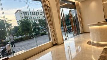 A hotel lobby with large windows, a reception desk, and a polished floor.