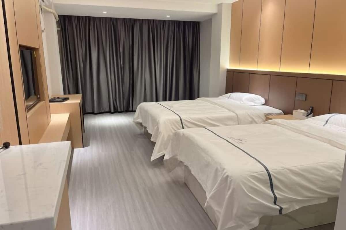 Een hotelkamer met twee bedden, een bureau en een groot raam met gordijnen.