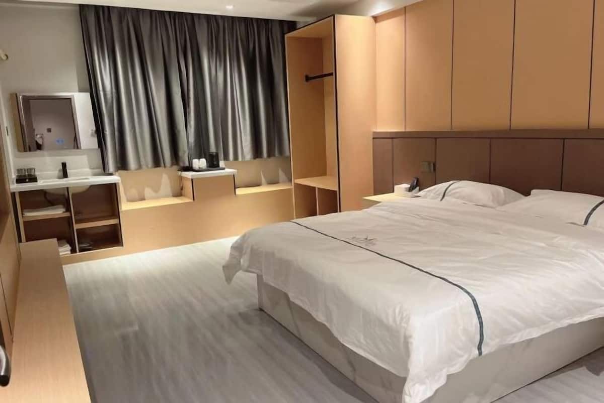 Een moderne hotelkamer met een groot bed, een kaptafel met spiegel en een zithoek met uitzicht op de stad.